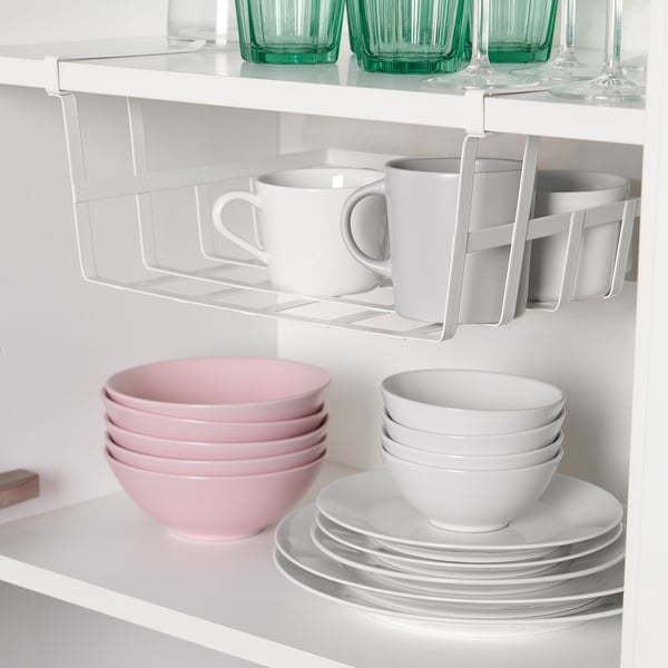 A kitchen cabinet with shelves showing a clip-on storage basket holding mugs, above stacked pink and white bowls and plates.