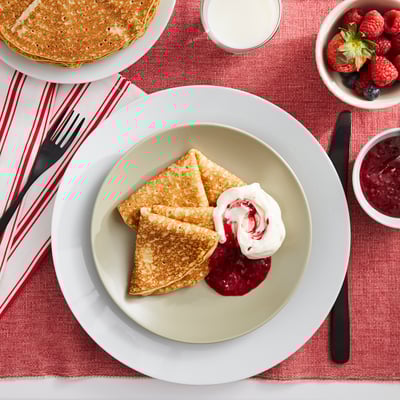 Plate of golden pancakes topped with cream and berry sauce on a red tablecloth.