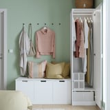A well-organized bedroom with a PAX wardrobe, featuring hooks for hanging clothes and accessories, and a bench with pillows and storage below.