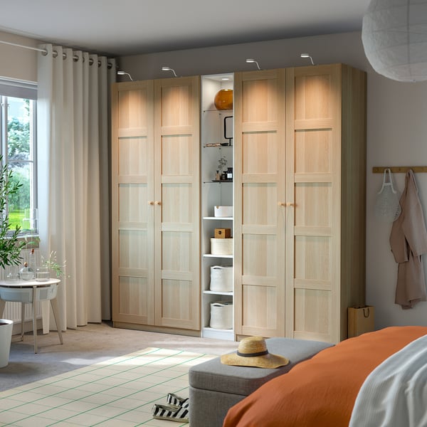 Large light wood PAX wardrobe with open shelves. It stands beside a bed with orange covers.