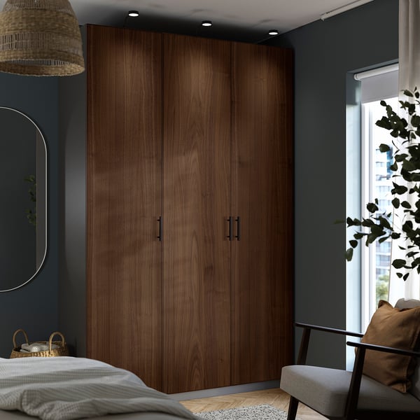 Modern bedroom with large wooden PAX wardrobe. Dark walnut, tall, sleek design. Includes chair and window.