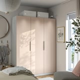 Modern bedroom with large beige PAX wardrobe, grey walls, natural light, and plants. Wardrobe is tall, closing closet doors.