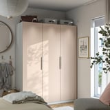 Modern bedroom with light PAX wardrobe, mirror, hooks, large window, and cozy chair with blanket.