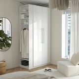 White PAX wardrobe, tall with shelves and hangers, fits corner, complements minimalist decor, larger than bed and chair beside it.