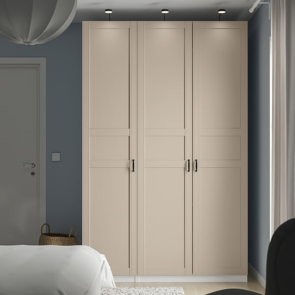 Beige PAX wardrobe against blue wall, flanked by bed and chair. Tall, sleek handles, subtle paneling.