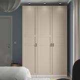 Beige PAX wardrobe against blue wall, flanked by bed and chair. Tall, sleek handles, subtle paneling.