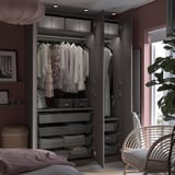 Modern black PAX wardrobe with mesh baskets and hanging sections against a mauve wall with soft lighting and a mirror.