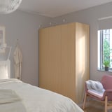 Modern bedroom with large IKEA PAX wardrobe, coat, and plant.