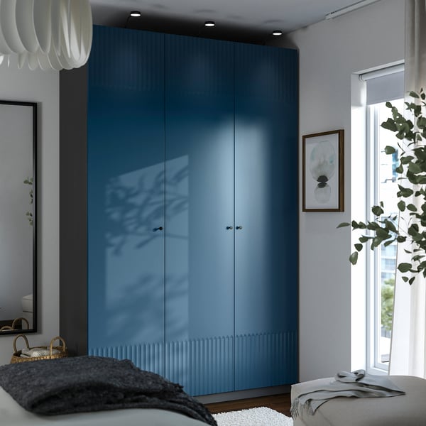 Modern bedroom with tall blue PAX closet, large windows, cozy seating, and decor.