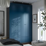 Modern bedroom with tall blue PAX closet, large windows, cozy seating, and decor.