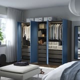 Bedroom with blue PAX wardrobe, hanging clothes, shelves, drawers, and a white bench.
