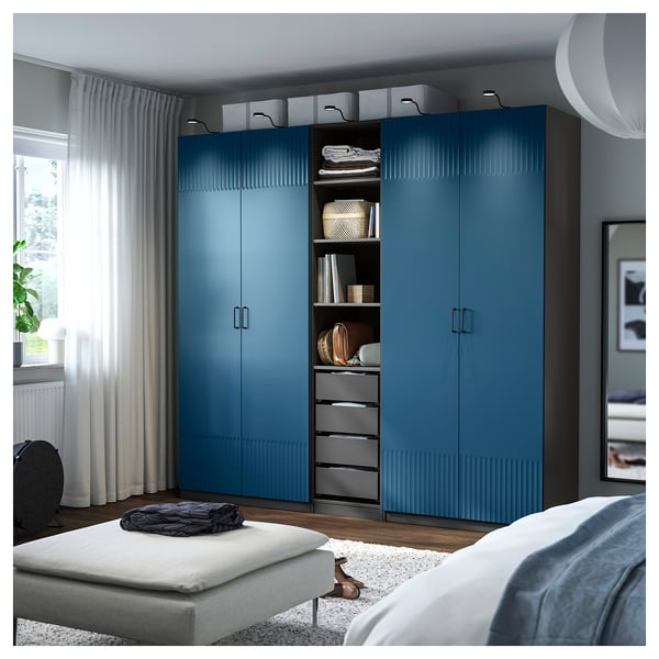 A blue PAX wardrobe with a textured door, standing tall beside a bed. It integrates shelves and drawers, offering ample storage.