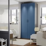 Modern bedroom with large blue PAX wardrobe against wall, white furniture, and large windows.