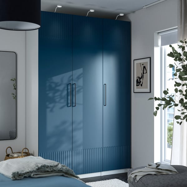 Modern bedroom with blue wardrobe, cozy bed by window.