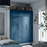 Large blue glossy wardrobe with handles, near window, bigger than bed, decorated with baskets and art.