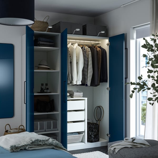 A blue PAX wardrobe with open doors revealing clothes, shelves, and drawers. Lighting highlights the organized interior.