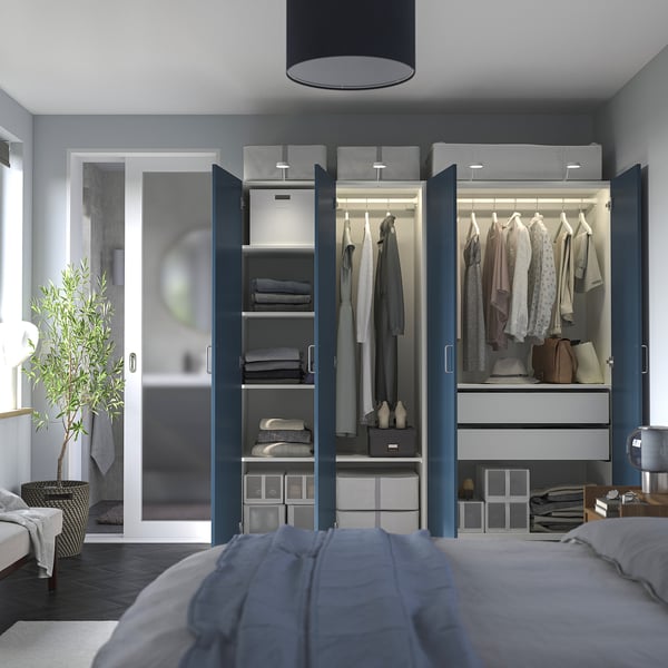 Modern bedroom with open blue wardrobe showing clothes and storage. Includes shelves, drawers, and hanging space. Lighting inside, clear decor.