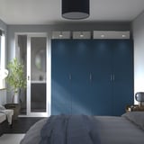 Modern blue PAX wardrobe against wall, larger than bed, with grey bedspread and sofa.