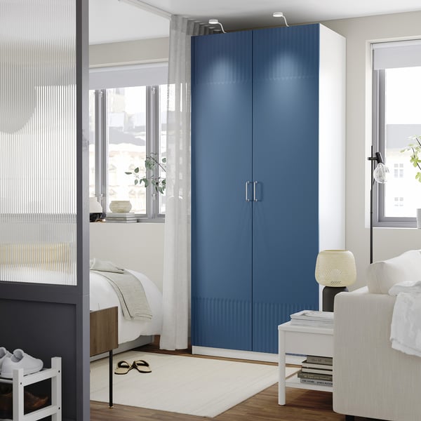 Modern bedroom with tall blue PAX wardrobe by window, minimal decor.