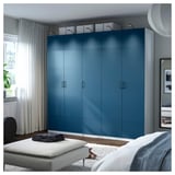 Teal PAX wardrobe with multiple doors and shelves, next to a window with a bench and blanket.