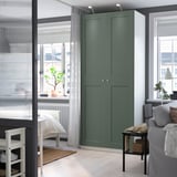 Modern room with large green PAX wardrobe, white bed, grey sofa, and several potted plants, creating a cozy and organized living space.