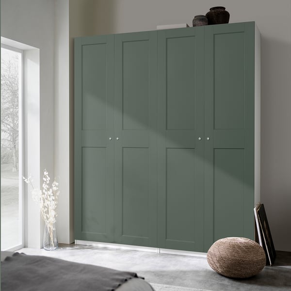 Modern bedroom with large teal PAX wardrobe, accompanied by a round woven stool and tall floral vase on the floor, offering ample storage space.