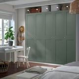 A large green PAX wardrobe with shelves and drawers. Above it is a desk with a white chair and a window with plants.