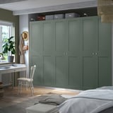 Modern bedroom with large PAX green wardrobes, white desk, & wooden chair; cozy & organized.