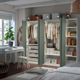 Modern bedroom with PAX wardrobe, open shelves, desk, chair, and window lamp.