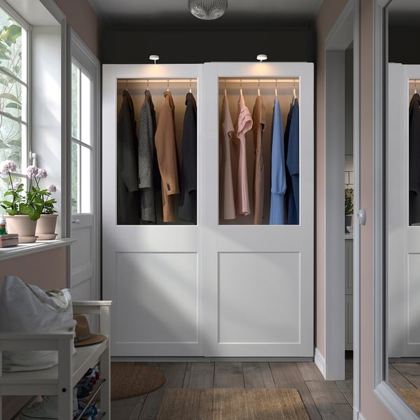 Large white PAX wardrobe with glass doors, displaying clothes, in a bright room.