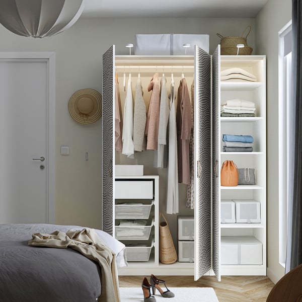 A modern bedroom with an open PAX wardrobe showcasing clothes hangers, shelves with folded clothes, and storage bins.