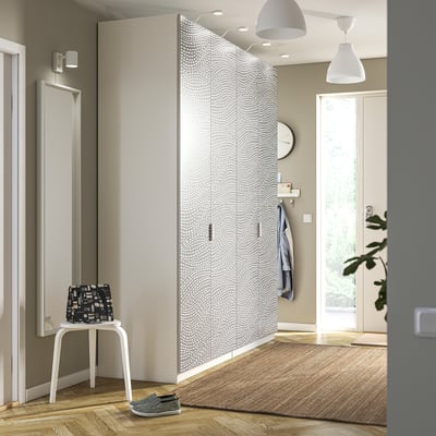 Modern tall white PAX wardrobe with wavy doors, standing near stool, mirror, and coats.