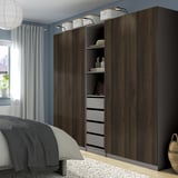 Modern bedroom with large dark wooden PAX wardrobe, tall, multi-compartment, integrated lighting, cozy, organized.