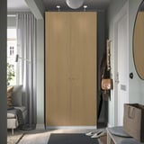 Modern light brown PAX wardrobe near white door, taller than gray chair and lamp.
