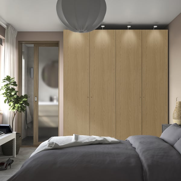 Modern bedroom with PAX wardrobe, soft lighting, large bed, and adjacent bathroom.