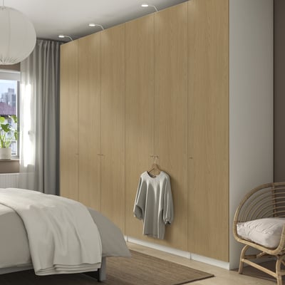Minimalist bedroom with PAX wardrobe, cozy bed, wicker chair, and hanging sweater.