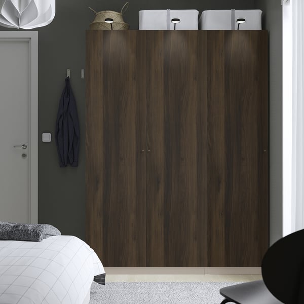 Modern bedroom with large dark wood PAX wardrobe. Wardrobe towers above bed, grey wall, white decor.