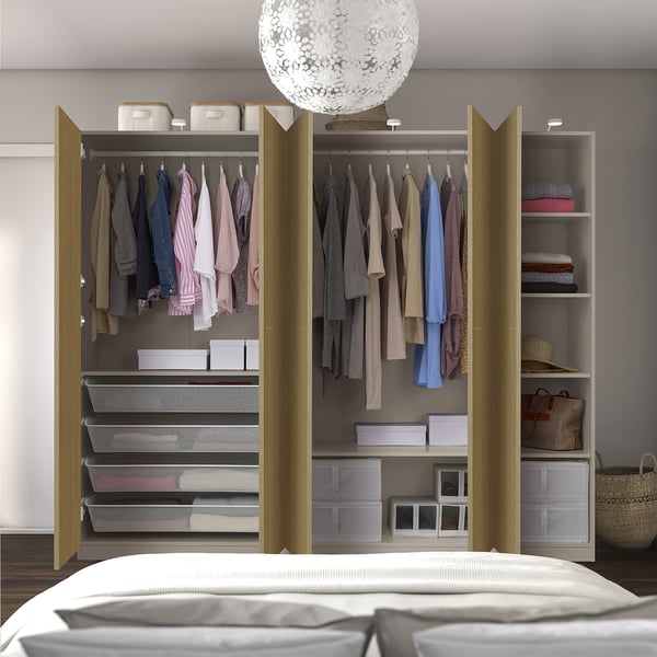 Open wooden wardrobe displaying organised clothes on hangers, shelves, and mesh drawers, with a lit, modern light fixture above.