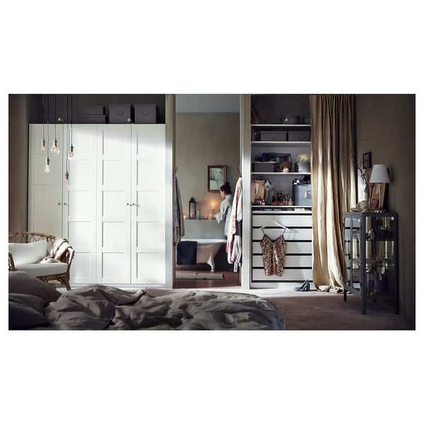 Modern bedroom with PAX white wardrobe, open shelves, and a bathtub. A woman lights a candle.