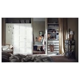 Modern bedroom with PAX white wardrobe, open shelves, and a bathtub. A woman lights a candle.