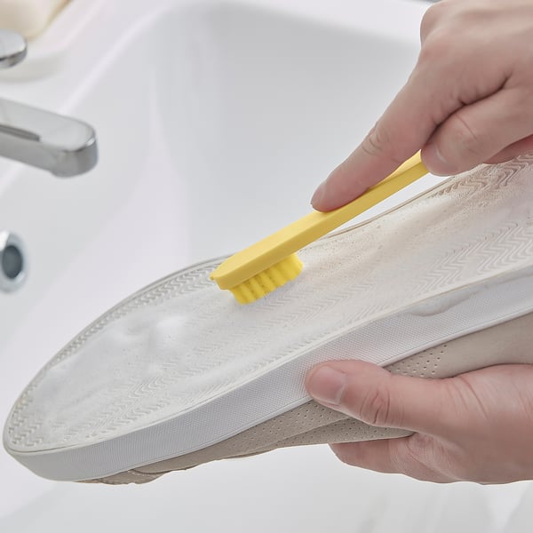 Person using small yellow brush to clean stains off white sneaker.