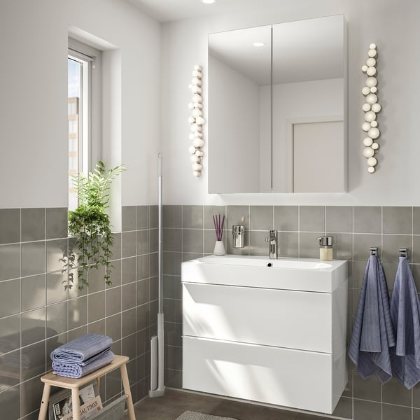 Modern bathroom with white sink, mirror, gray tiles, blue towels, plant, and mop.