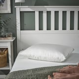 PILSPINNARE pillow in white against green quilt, plush, comfy, on headboard.