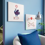 Two vibrant canvas prints on blue wall. Chair, lamp, plant below. Cozy room decor.