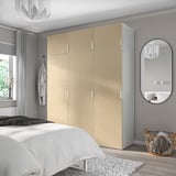 Large wooden wardrobe beside a white bed, mirrored side, gray walls.