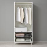 A white PLATSA wardrobe with hanging shirts and baskets, storing clothes and accessories.