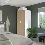 Green bedroom with white bed, PLATSA wardrobe, tall plant.