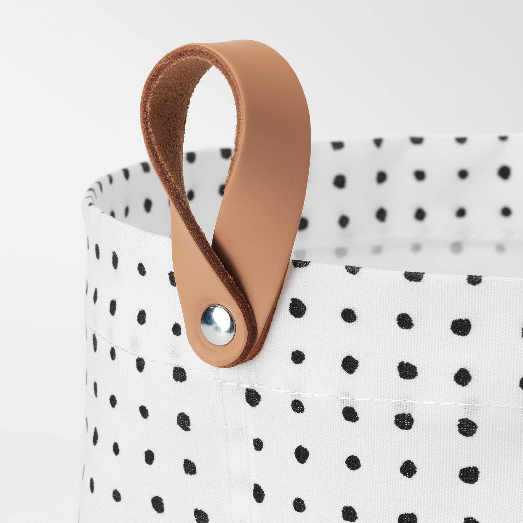 White fabric basket with black polka dots, sturdy tan leather handle.