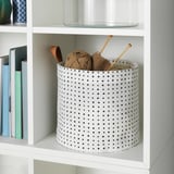 White shelf with polka dot basket holding yarn and knitting needles.