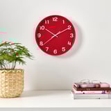 Red wall clock with white hands and silent quartz. Wicker plant and books above.